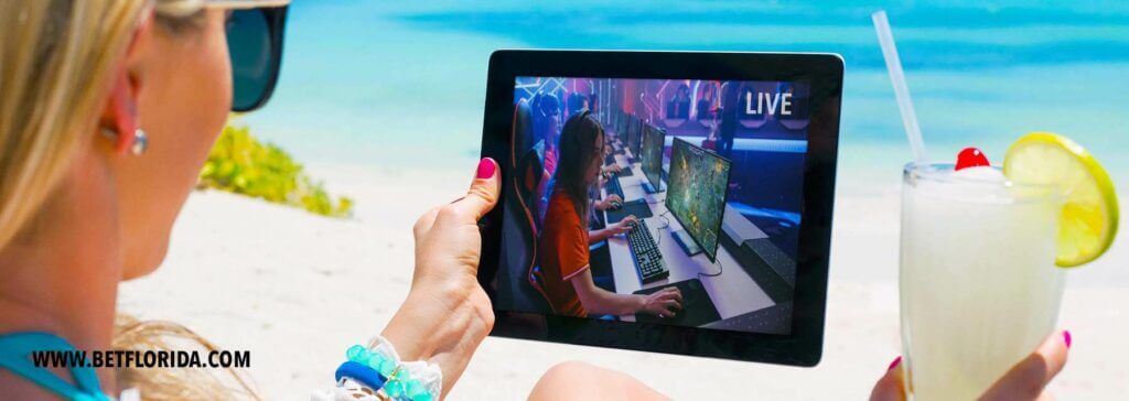 woman holding tablet, watching esports with a drink on the beach